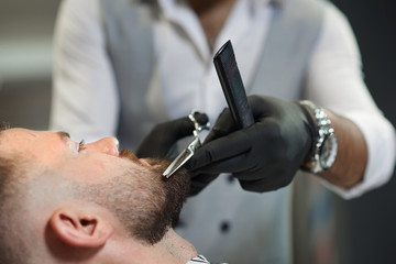 Closeup of process of cutting beard of client in barber shop