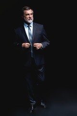 Full length portrait of Mature business man wearing formal suit standing on black background.