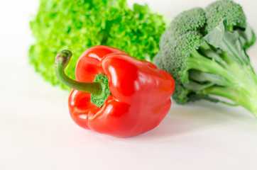 Juicy red pepper with a green tail lies next to Bundle of lettuce and broccoli are on a white background
