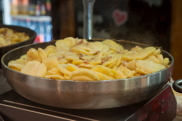 closeup of sliced potatoes cooking in big stove at the christmas market