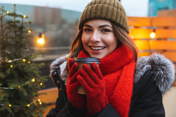 Happy young woman standing posing outdoors winter concept drinking coffee.