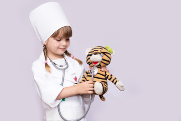 Smiling little girl playing doctor and listening teddy bear with stethoscope isolated