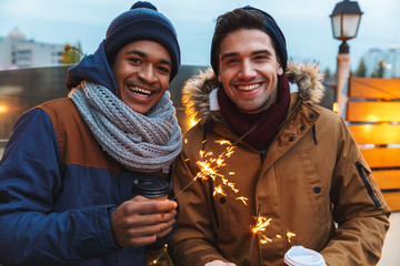 Happy excited young men friends standing posing outdoors winter concept drinking coffee holding...