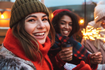 Young friends talking with each other drinking coffee outdoors winter concept holding bengal lights.