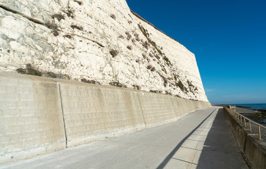Fototapeta premium Saltdean beach seafront and white sandstone chalk cliffs with two local people walking for exercise. Undercliff walkway at East Sussex Brighton marina, UK.