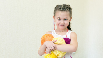 A girl with balls of thread for knitting. The little girl holds knitting yarns in her hands, and the yarn hangs on her head.