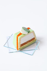Piece of Contemporary Green Tea Mousse Cake with tropical fruits, on white background.