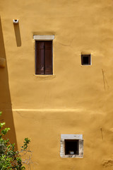 Yellow colorful house wall and windows with wooden shutters. Beautiful travel picturesque background