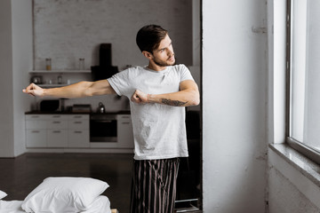 young man in pajamas exercising and looking at window in the morning