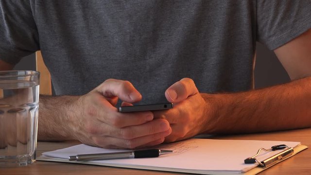 Close up of male hands using smartphone at office desk over clipboard notepad