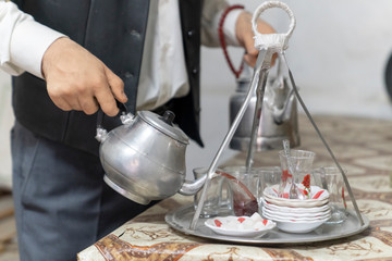 Fototapeta na wymiar Hands of man (tea maker) with metal Turkish teapot pouring tea into glass cups in a coffee house in Turkey