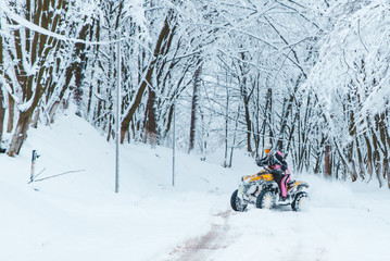 two persons ride quad bike in snowed forest