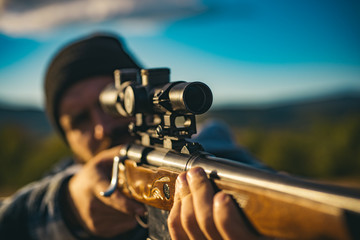 Close up snipers carbine at the outdoor hunting. Hunter aiming rifle in forest. Hunter with shotgun...