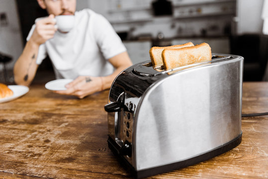 cropped shot of young man drinking coffee at home with toaster on foreground