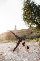 Woman practice yoga in the nature at sunset on sand beach against of lighthouse