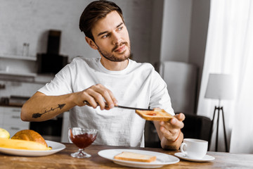 Fototapeta na wymiar handsome young man applying jam onto toast at home