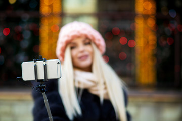 Glamor blonde girl wearing pink cap, taking selfie on city street decorated with garlands. Space for text