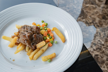 Grilled pork steak with French fries and vegetables on a white