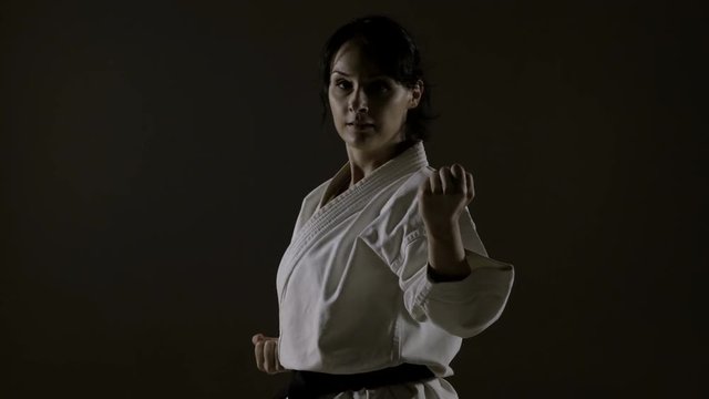 girl practicing karate, wearing kimono, harsh side light against black background