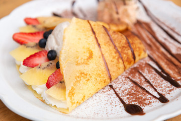 Side view of Cold crepe with vanilla ice cream, strawberry, kiwi and whipped cream topped with chocolate sauce on the wooden table. (Selective focus with shallow depth of field)