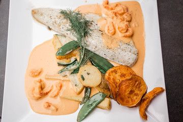 Delicious Dutch food in the restaurant close to the Scheveningen Beach in The Hague, The Netherlands. Beautiful fish with vegetables chips, shrimps sauce, salad, french fries and beer.