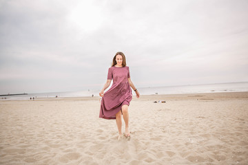 Fototapeta na wymiar Young beautiful brunette woman in burgundy dress dance on the Scheveningen Beach in The Hague, The Netherlands.