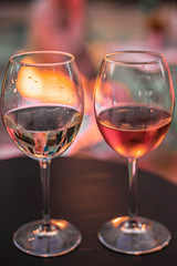 Two glass of wine on the table on the colorful lights background. Glass of white wine and glass of pink wine close up.