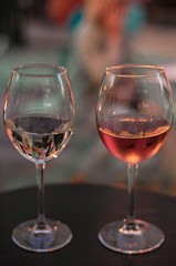 Two glass of wine on the table on the colorful lights background. Glass of white wine and glass of pink wine close up.