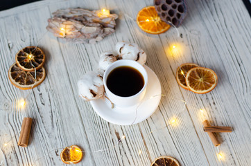 A cup of coffee with cotton and oranges on a wooden background.