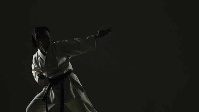 karate girl practicing jump kick, wearing kimono, on dark background. slow motion recorded at 120fps