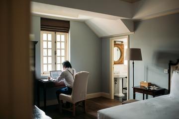 Back view of businessman with suspenders working on a laptop at hotel room.