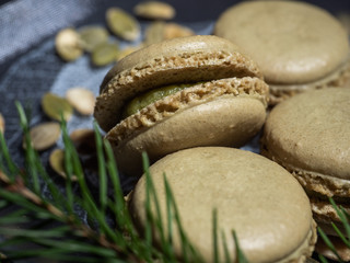 Fototapeta na wymiar Pistachio macaroons on a glass plate against a dark background, a scattering of pumpkin seeds. Spruce branch. Close-up.