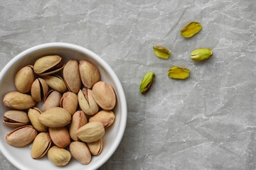 Salted and peeled pistachios in a white deep plate on a light background