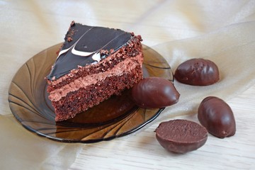 A piece of delicious chocolate cake on a brown plate and chocolates.