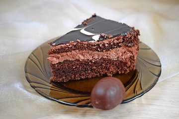 A piece of delicious chocolate cake on a brown plate and chocolates.