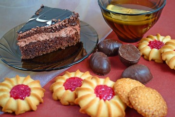 A piece of delicious chocolate cake and cookies with strawberry jam for tea.