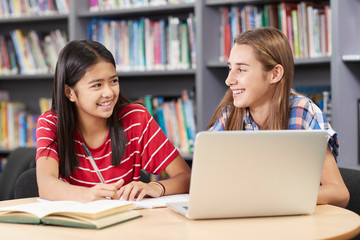 Two Female High School Students Working At Laptop In Library