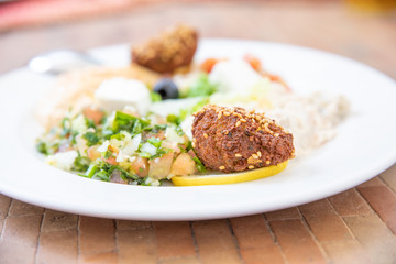 falafel (fried ball with chickpeas or fava beans) in white dish with mezze or meze, selection of typical Arabic appetizers (hummus, baba ghanoush, Feta cheese, Marrakesh salad, tabule, olives)