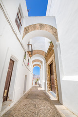 Naklejka premium vertical shot of narrow pedestrian famous street with archs, in typical white houses Andalusian village named Vejer de la Frontera (Cadiz, Andalusia, Spain, Europe)