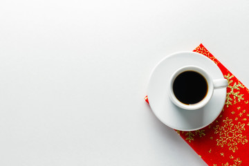 A cup of coffee on a saucer on a bright Christmas napkin on a white background. Flat lay. Top view, Copy space