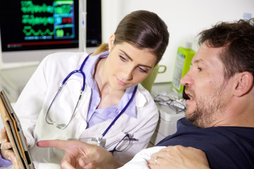 Doctor showing results of test on tablet to worried patient in hospital