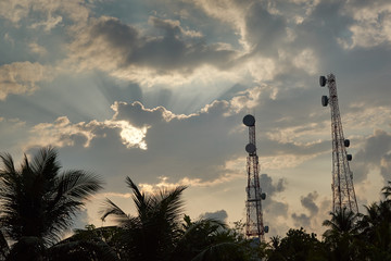 Two Antenna Towers Reaching High Into The Cloudy Sunny Morning Sky Surrounded By Coco Palm Trees On...