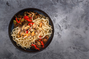 Traditional Asian food - noodles with seafood, salad, red pepper and fried mushrooms are on a gray table. Copy space. Top view