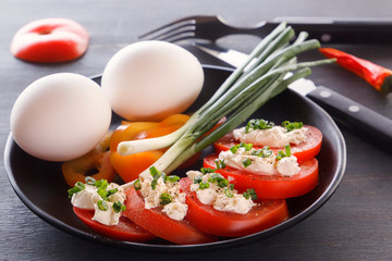 Sliced tomatoes with cheese and herbs in a black plate with onions, sweet peppers and eggs. Close-up