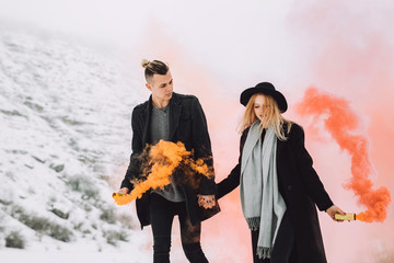 Girl holding a red smoke bomb in the forest.Boy holding orange smoke in his hands.The guy is looking at his beautiful young girl.