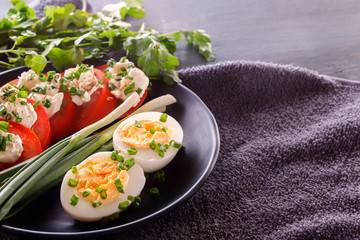 Half boiled eggs with tomatoes, green onions, sprinkled with greens in a black plate on a gray wooden table. Close-up. Copy space