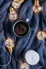  Cup of coffee , candle and warm woolen sweater , decorated with led lights.Winter and Autumn weekend concept. Flat lay, top view.