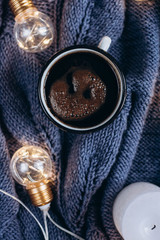  Cup of coffee , candle and warm woolen sweater , decorated with led lights.Winter and Autumn weekend concept. Flat lay, top view.