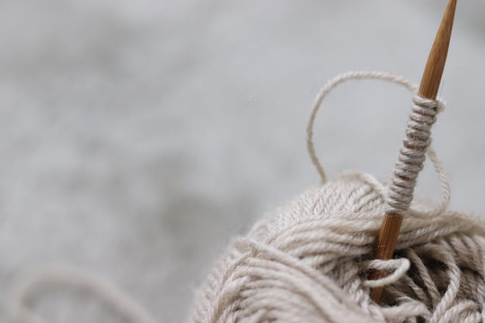 Close Up Of Skein Of Wool Yarn And Knitting Needles With Piece Of Hand Knitted Textile On Blanket