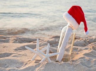 Santa hat on message in a bottle with white starfish in beach sand